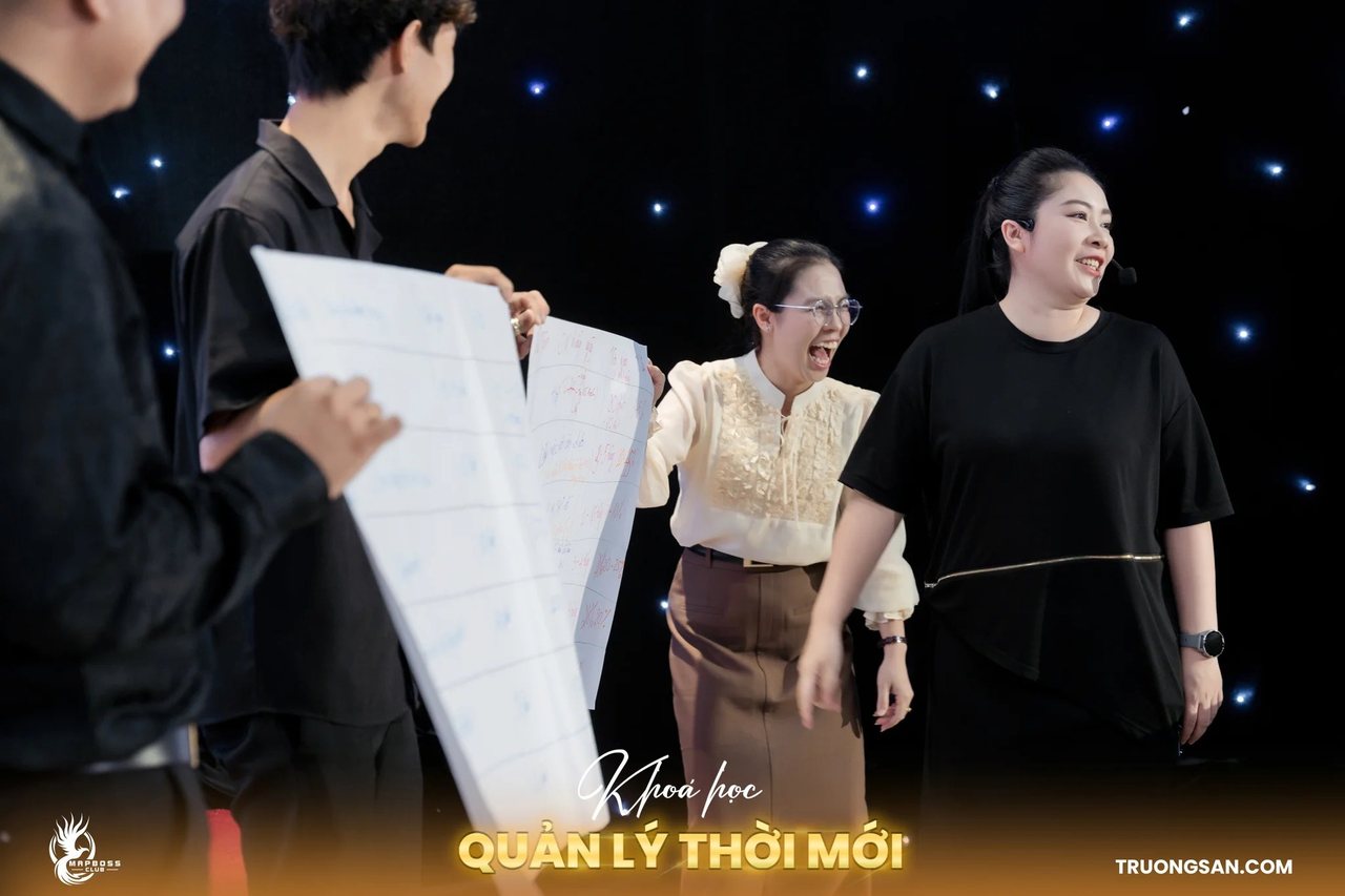 Học viên Quản Lý Thời Mới giơ tấm giấy khổ lớn, người đứng cạnh cười lớn