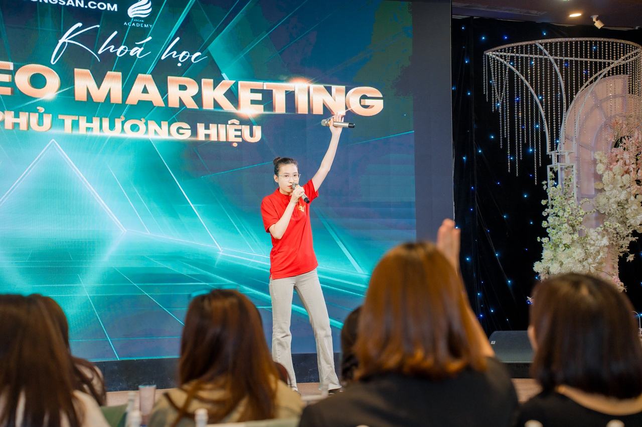 Nữ học viên áo đỏ lớp Video Marketing mùa 11 giơ tay nói trên sân khấu