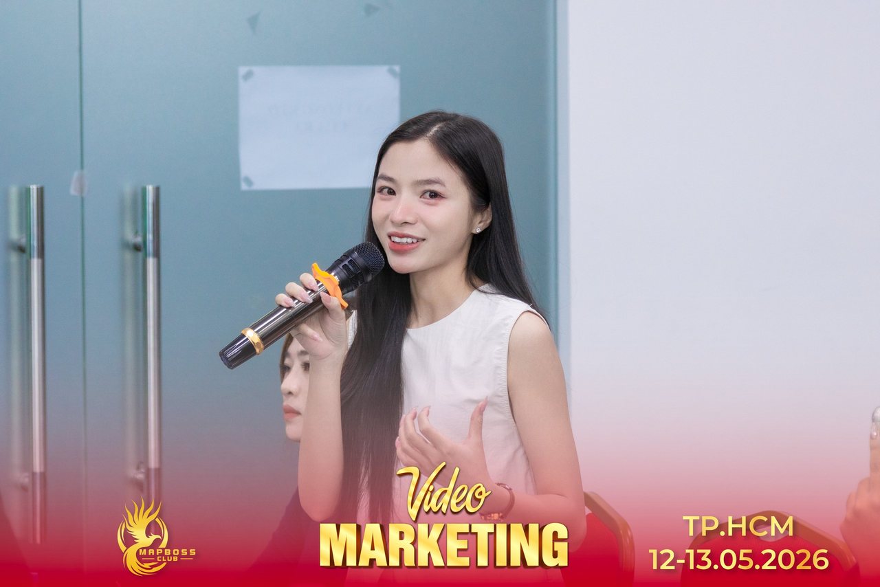 Nữ học viên Video Marketing mùa 12 mỉm cười cầm micro chia sẻ trước lớp