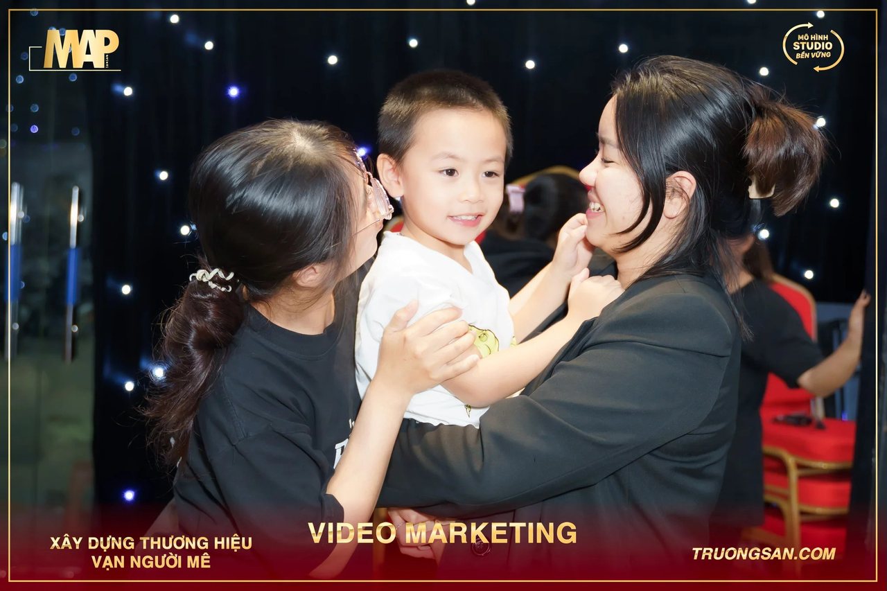 Hai học viên Video Marketing mùa 6 bế và trêu đùa một cậu bé giữa lớp